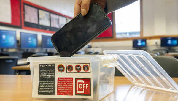A student places a mobile phone in a box before the start of a lesson. 