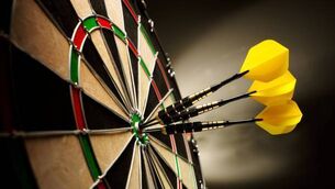 <p>Three yellow darts hitting the target in a game of darts scoring a bulls eye. </p>